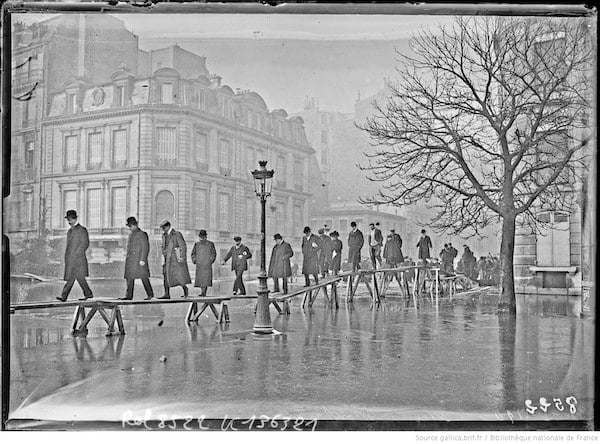 31-1-1910, avenue Montaigne [Paris, 8e arrondissement, file de personnes marchant sur des planches sur pilotis, inondations] : [photographie de presse] / [Agence Rol]